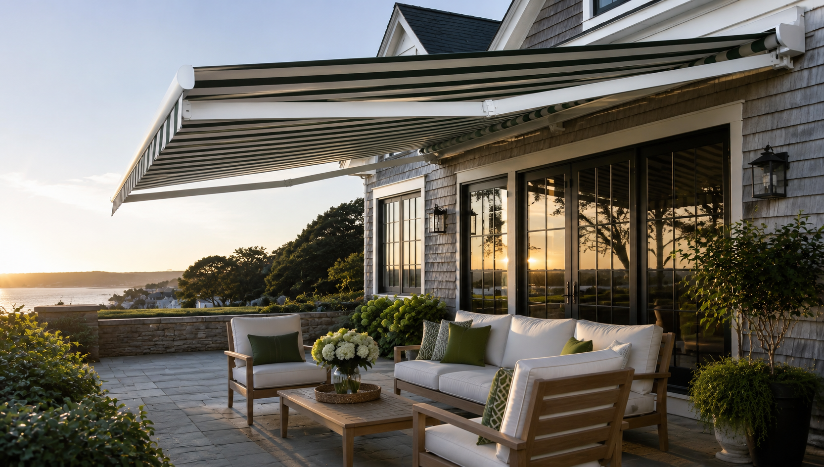 Green and cream striped retractable patio awning extended over a stone patio lounge at a shingled waterfront home