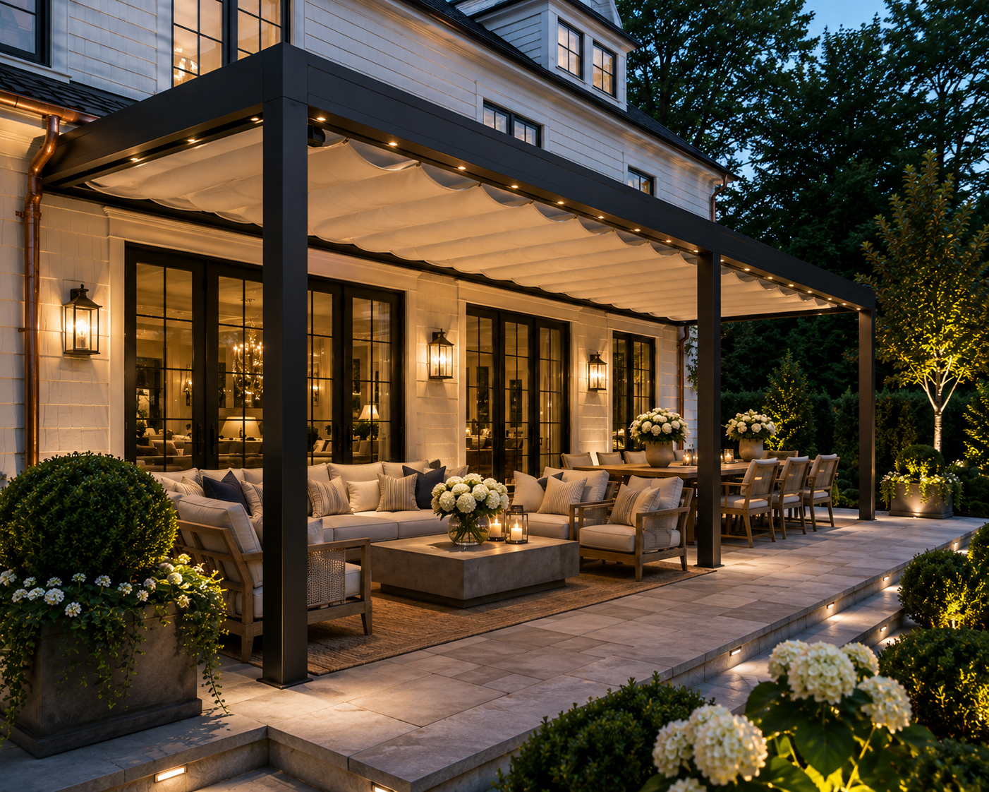 Black aluminum pergola with a draped cream retractable fabric roof over an illuminated evening patio